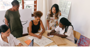 Image of diverse people sitting and standing around a table while working