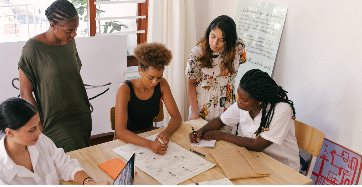 Image of diverse people sitting and standing around a table while working