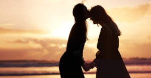 Silhouette of two people holding hands and one kissing the forehead of the other